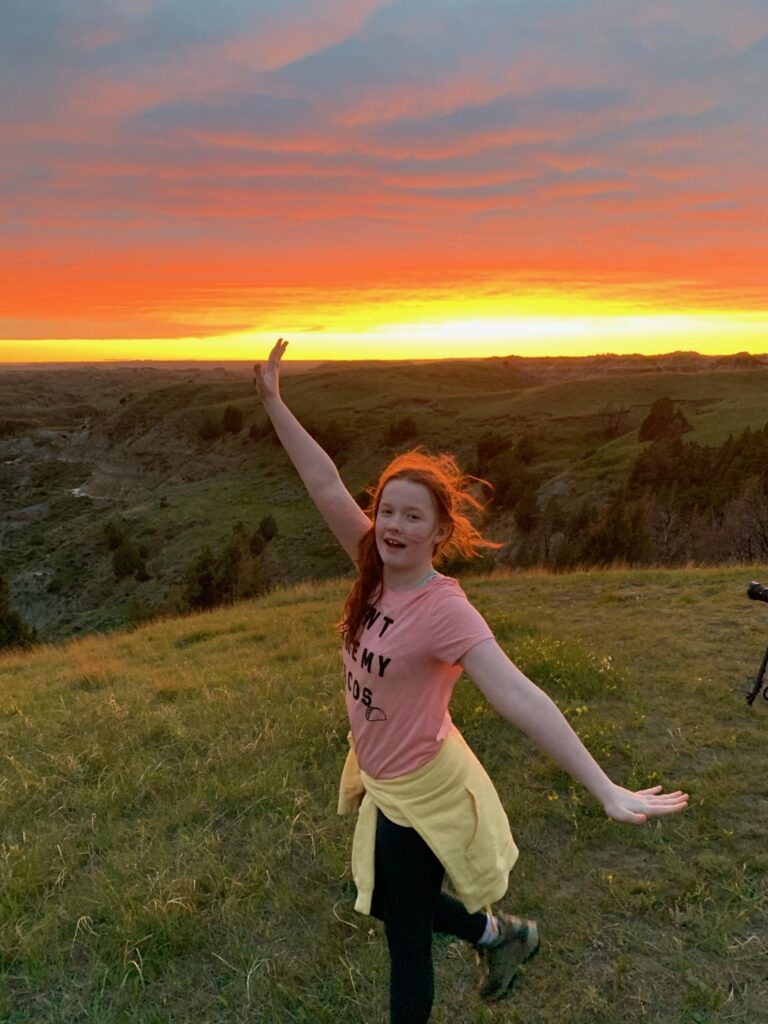 Cameron posing during a amazing red sunset, her hair glowing red with the last light of day at the Boicourt Overlooking, looking down on the  Little Missouri Badlands.