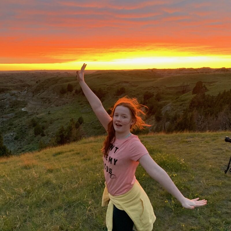 Cameron posing during a amazing red sunset, her hair glowing red with the last light of day at the Boicourt Overlooking, looking down on the Little Missouri Badlands.