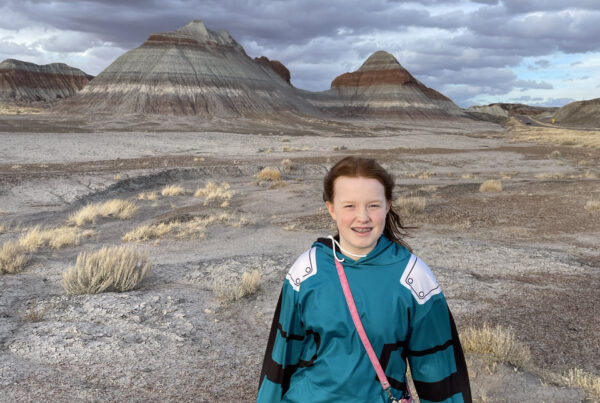 Cami standing at the start of the Historic Blue Forest Trail, with storm clouds looming over the buttes behind us.