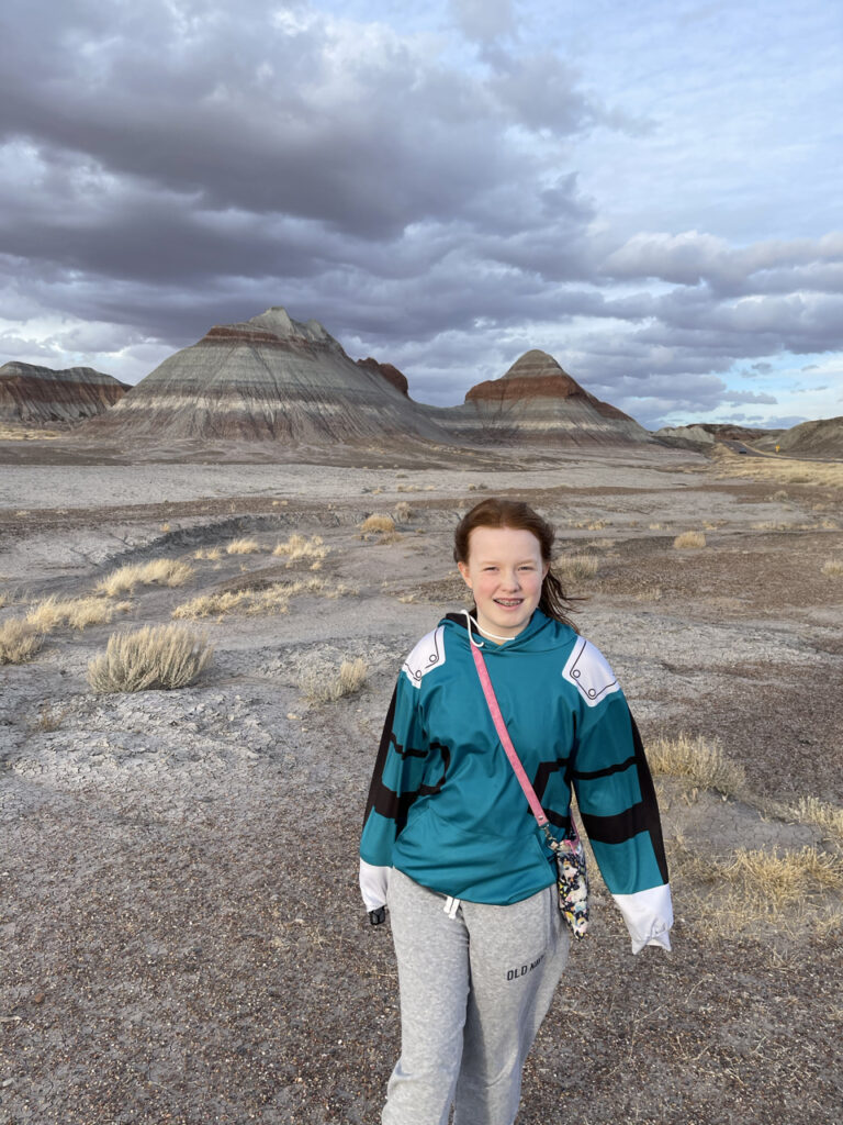 Cami standing at the start of the Historic Blue Forest Trail, with storm clouds looming over the buttes behind us.