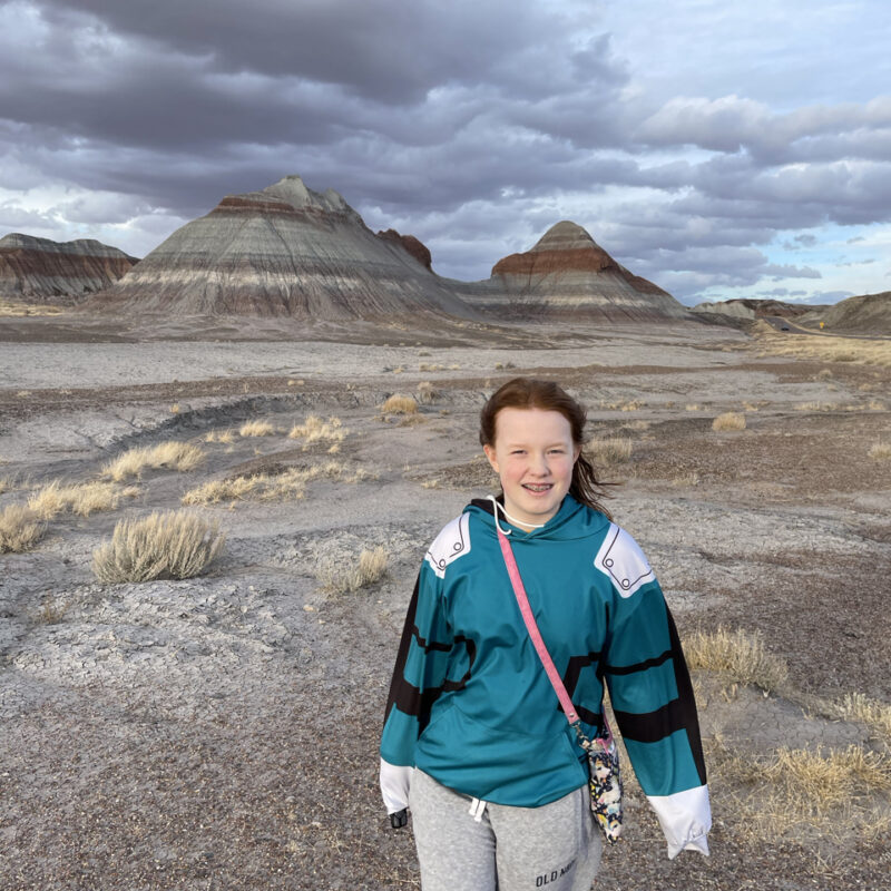 Cami standing at the start of the Historic Blue Forest Trail, with storm clouds looming over the buttes behind us.