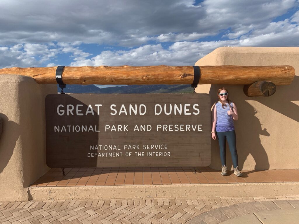 Cameron standing in front of the park sign for Great Sand Dunes National Park and Preserve in Colorado.