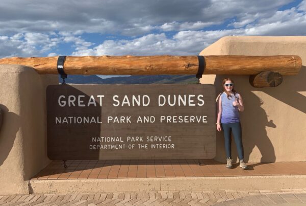 Cameron standing in front of the park sign for Great Sand Dunes National Park and Preserve in Colorado.