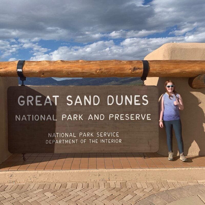 Cameron standing in front of the park sign for Great Sand Dunes National Park and Preserve in Colorado.