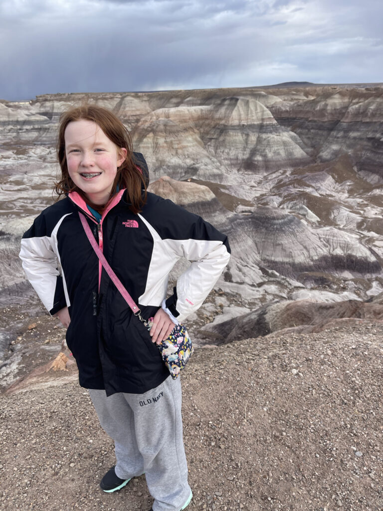 Cameron standing and smiling on top of the badlands, behind her is a stunning valley of mountains and rocks.  In the Petrified Forest National Park.