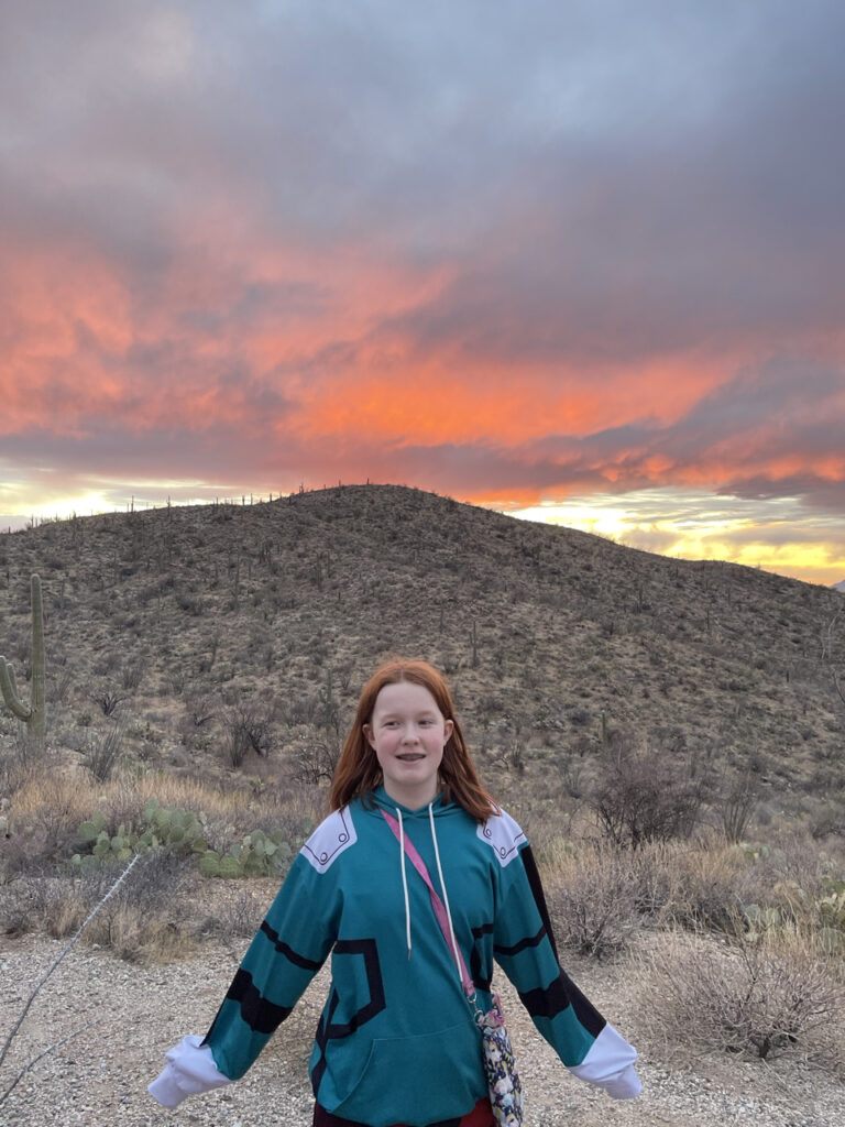 Cami standing on the mountain side at Sunset with a bright red sky behind her on the east side of Saguaro National Park in the Rincon Mountain District.