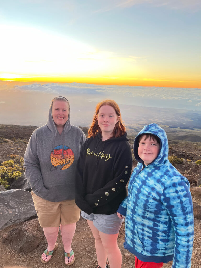 Cat, Cameron, and Collin watching sunset from a lookout in Haleakala National Parks. The clouds had inverted and they are below us, and the sky is bright yellow. 