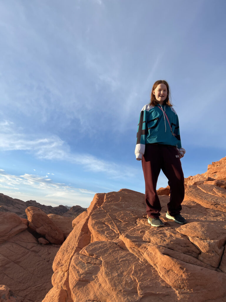 Cameron standing on red glowing rocks from the sunrise light at the Valley of Fire state park. She is up very high on the rocks admiring the view.