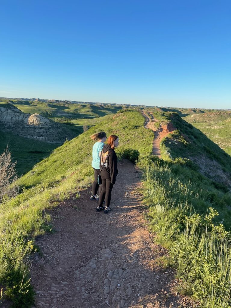 Cat and Cameron making their way across a trail the top of the badlands on a bright blue sky day.