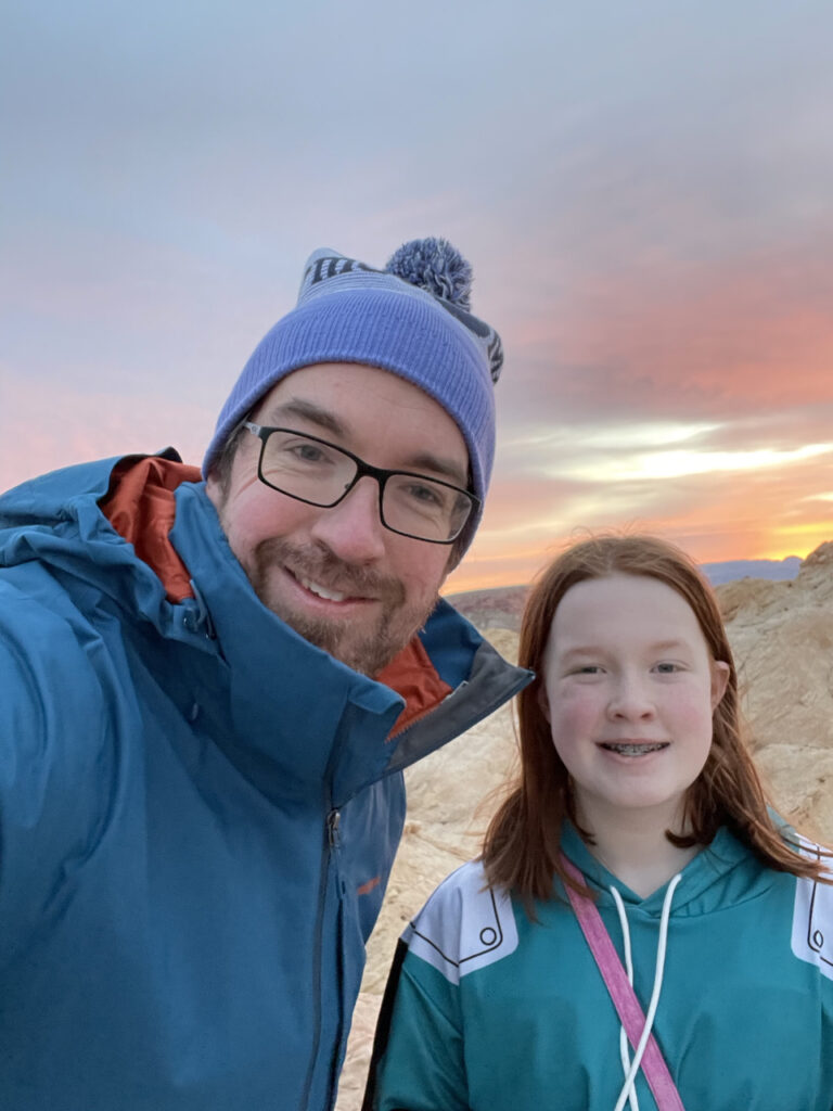 Myself and Cameron standing in the Valley of Fire State Park at sunrise. The sky is lite up with color and we are both bundled up for the chilly morning in the desert.