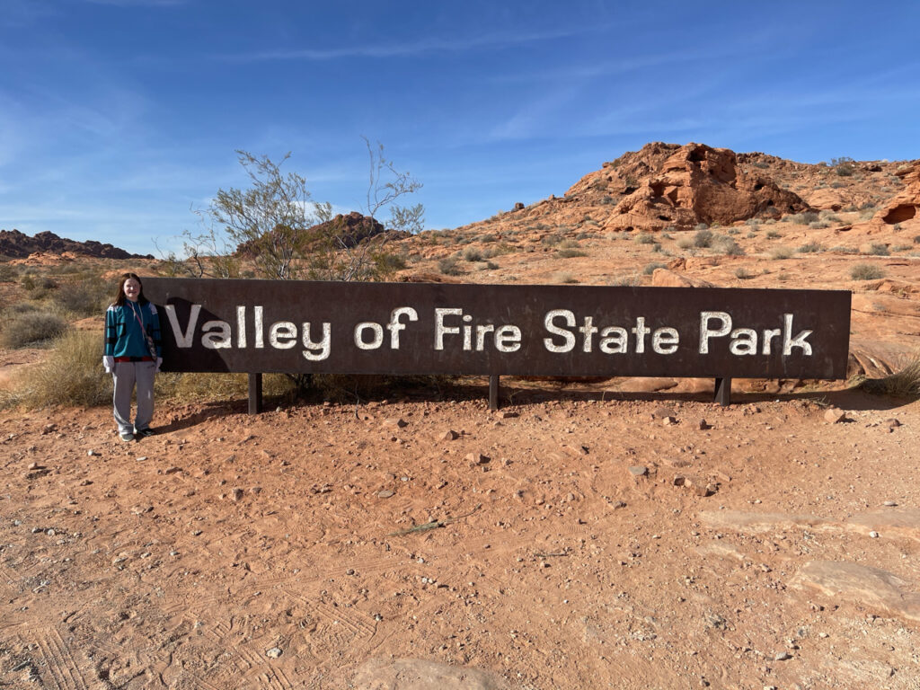 Cameron standing in front of the valley of Fire State Park sign mid day in the middle of the desert outside of Las Vegas.