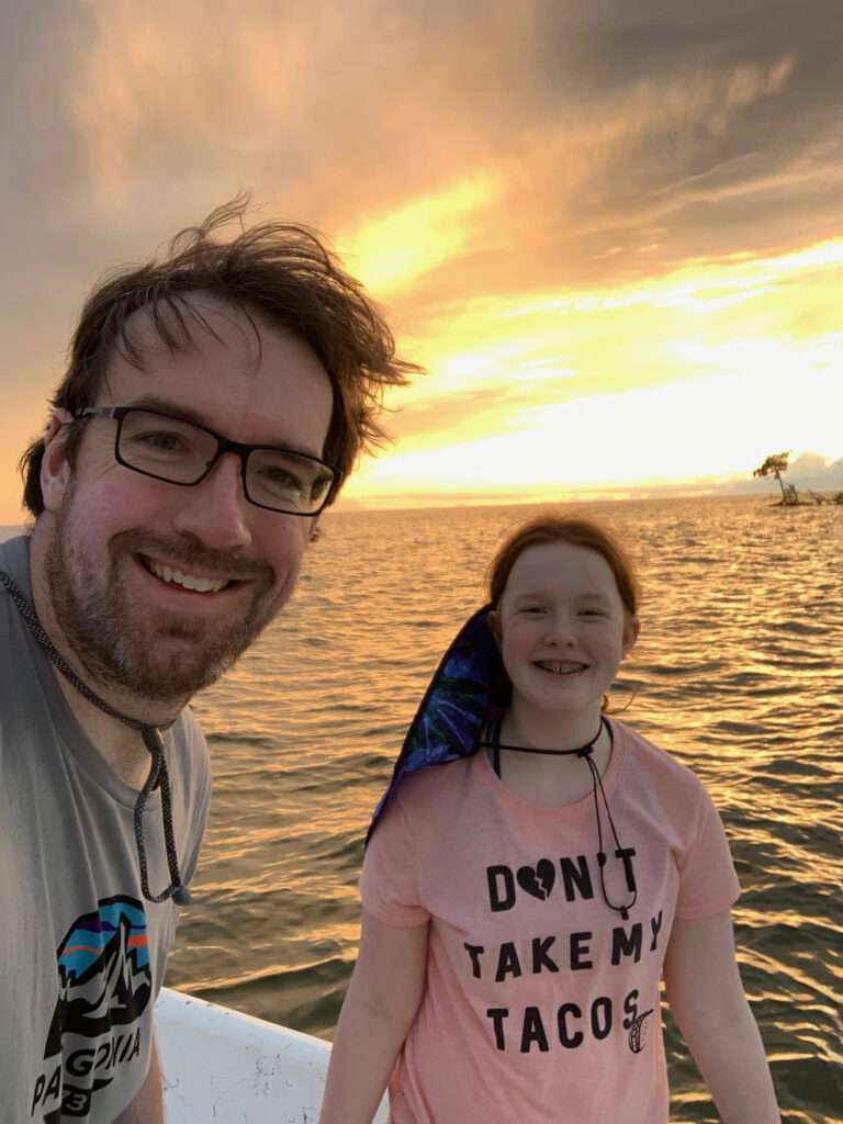 Cameron and myself on a boat in the Ten Thousands Islands area of the Everglades at sunset with the sky and the ocean both bright with color. 