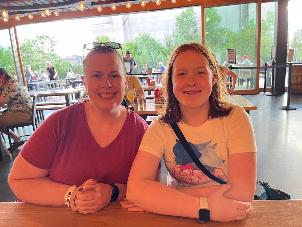 Cat and Cami sitting at a large indoor - outdoor table at Surly Brewing Co.