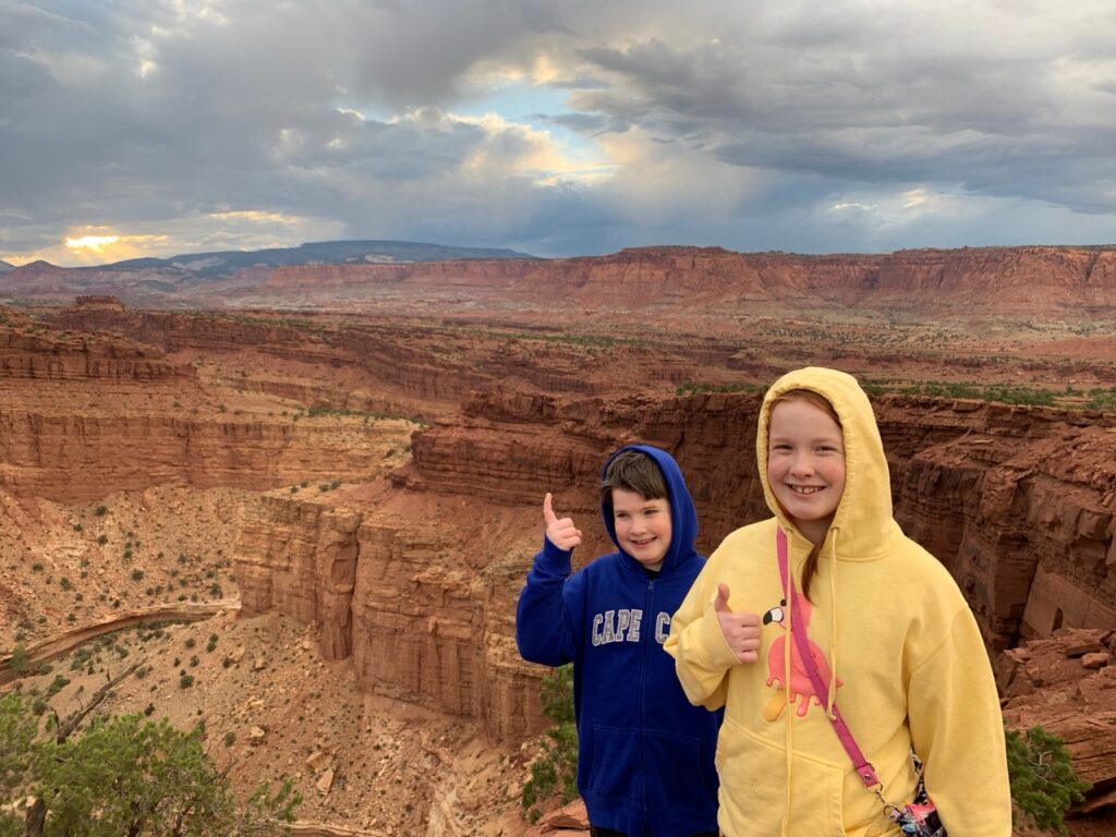 Collin and Cameron at Goosenecks Overlook at sunset with storm clouds in the distance. In Capitol Reef National Park.