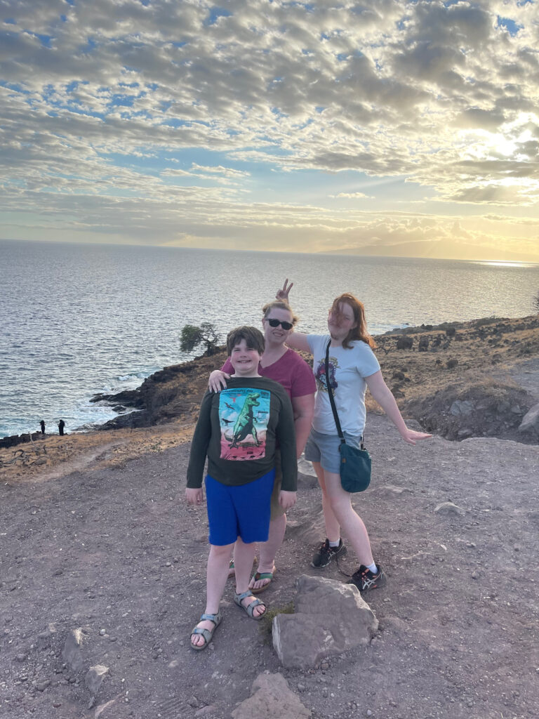 Cat, Cameron and Collin all smiles standing near the cliffs edge looking over the Pacific Ocean at sunset off a random point on a road in Maui - Hawaii.