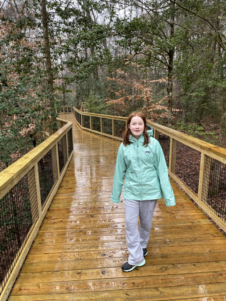 Cameron in her rain gear, starting her walk on the very wet boardwalk on the Firefly Trail in Congaree National Park.