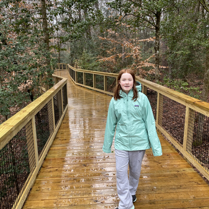 Cameron in her rain gear, starting her walk on the very wet boardwalk on the Firefly Trail in Congaree National Park.