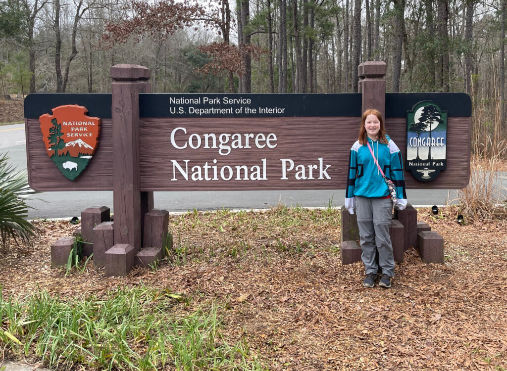 Cameron standing in front of the Congaree National Park Sign in the middle of winter.