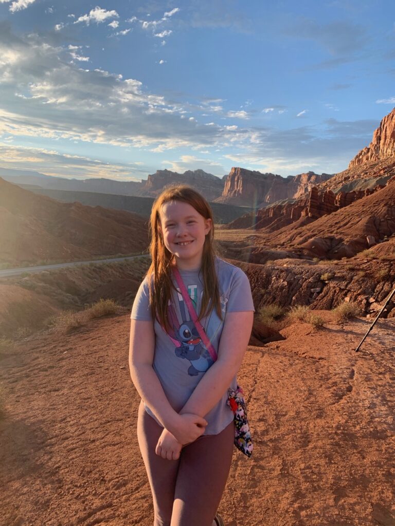 Cameron waiting with me for sunset on some rocks next to the Slickrock Divide. The sun has amazing soft red light shining down on the mountains in the distance and the winding  scenic drive road can be seen in the foreground.