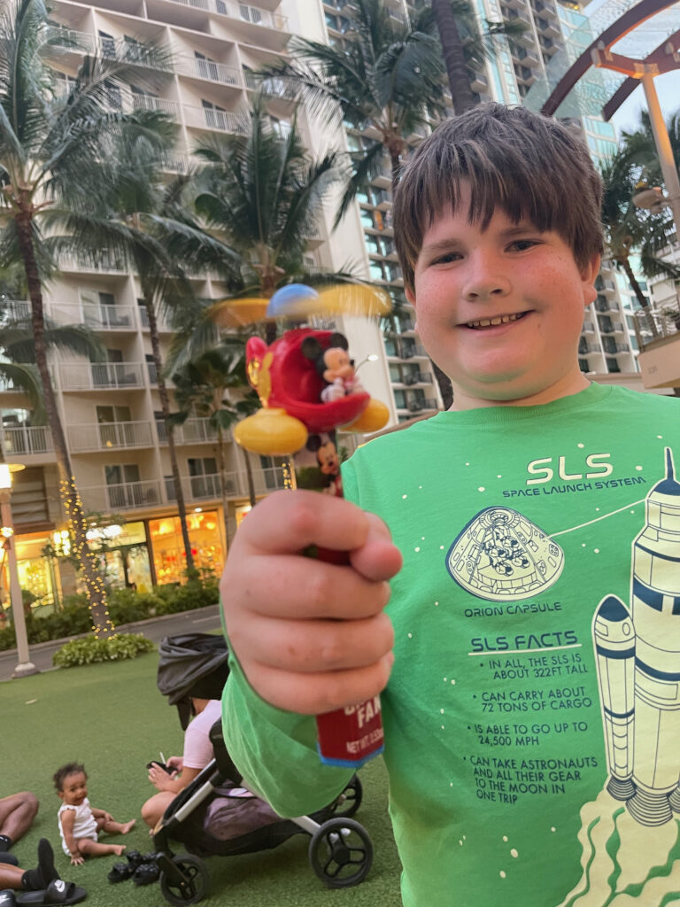 Collin standing outside in a city park, in Waikiki showing off his new mickey mouse fan toy.