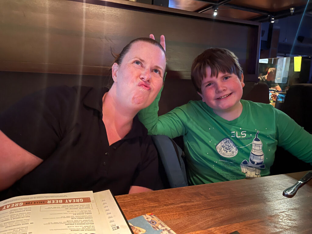 Cat looking up and making a funny face, while Collin smiles and gives Cat bunny ears sitting in a restaurant booth in Waikiki.