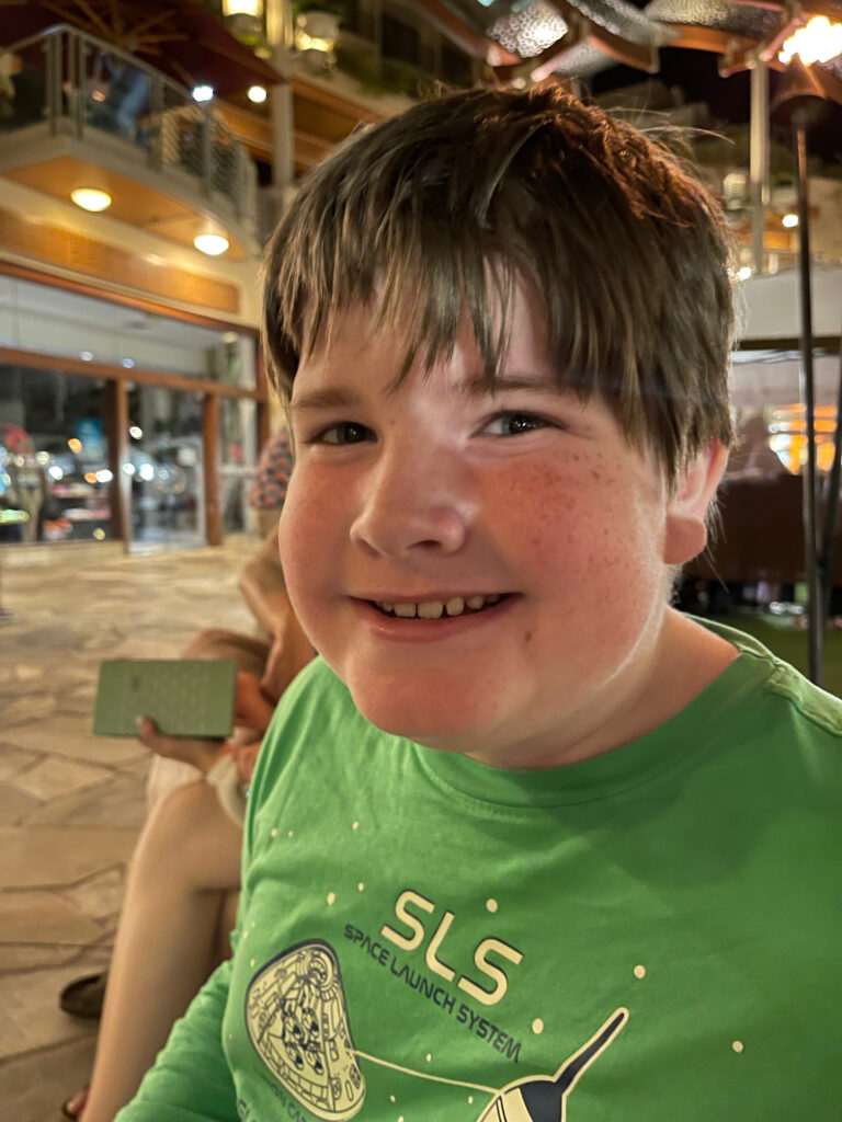 Collin smiles at night in Waikiki with his face light from the city lights.