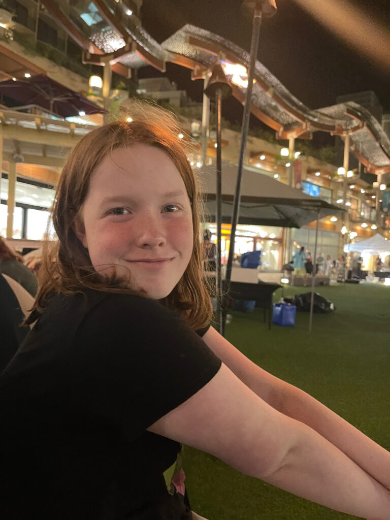 Cameron sits on the ground in a small part in the middle of all the shops of Waikiki at night.