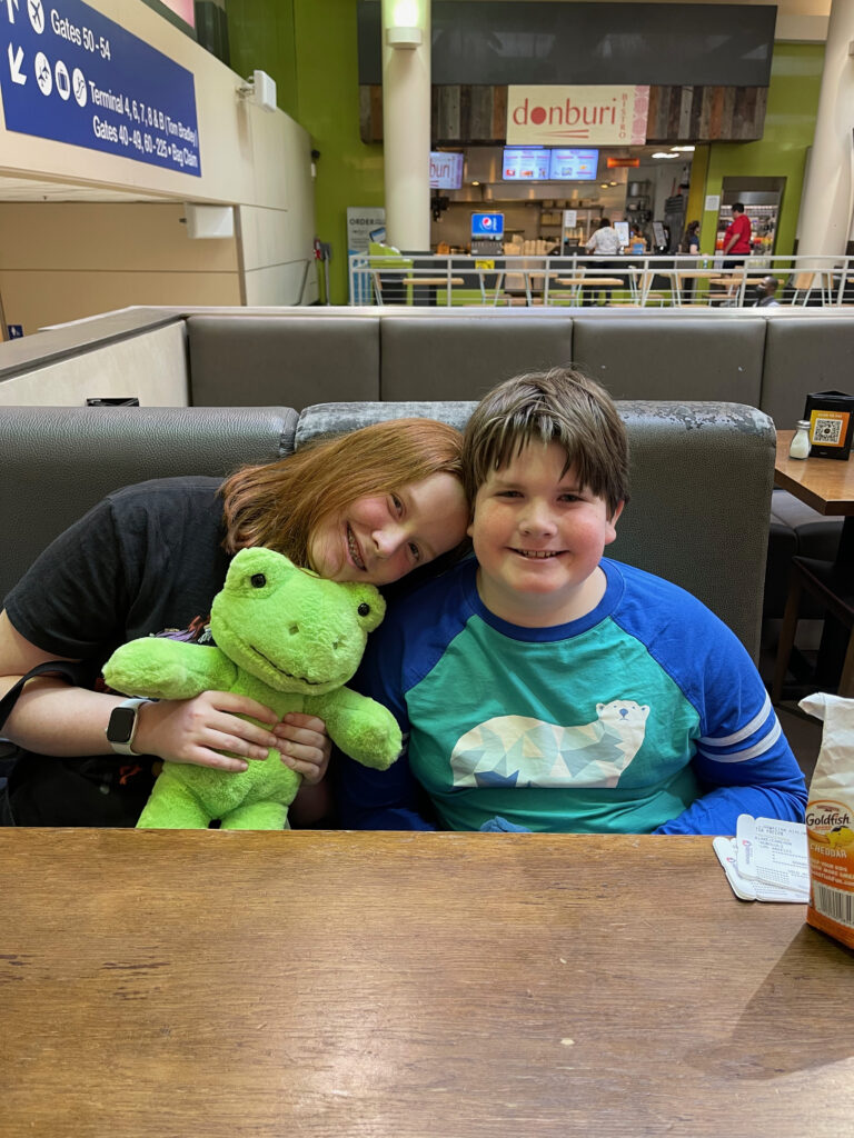 Cameron sitting in a booth with Collin leaning over on her, while holding her teddy bear. Waiting for breakfast in the LAX airport. 