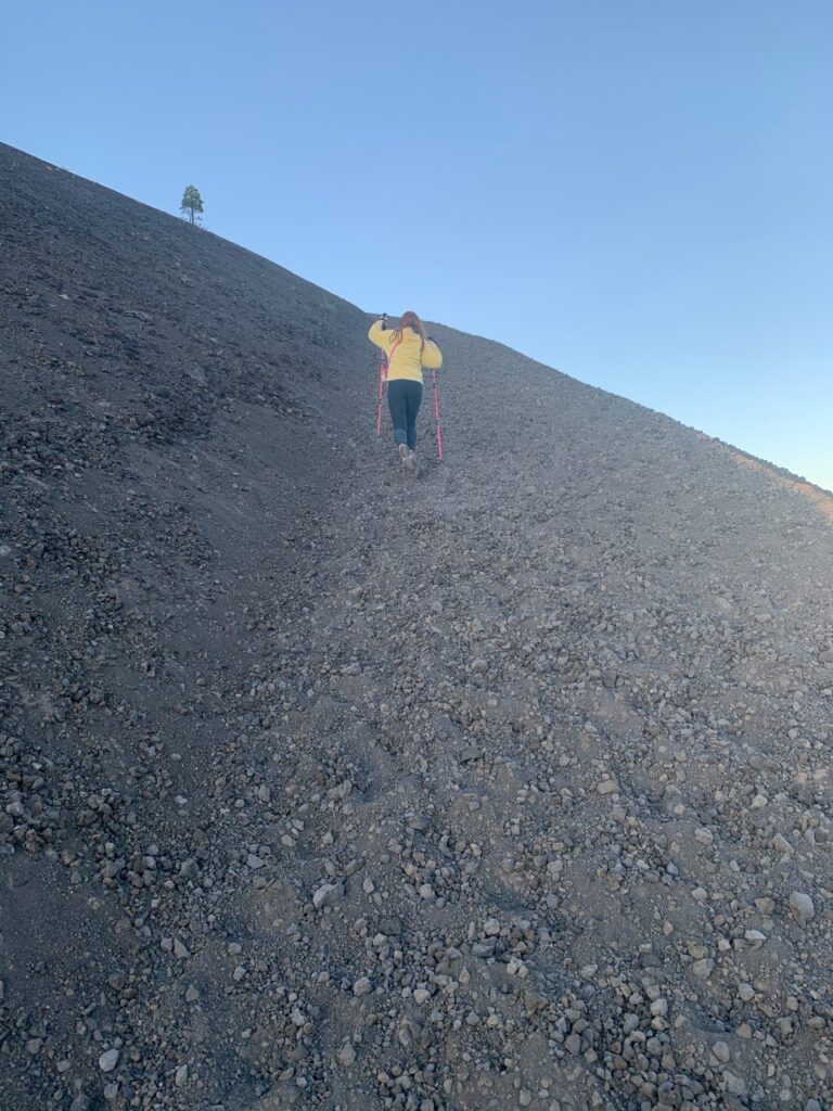 Cameron hiking up the very steep trail on the side of the Cinder Cone Volcano, using hiking poles and taken just after dawn.