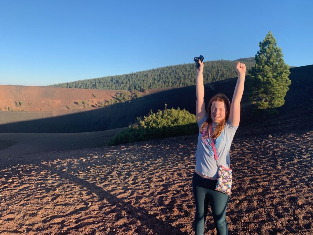 Cameron celebrating at the top of the hike on the Cinder Cone Volcano in Lassen.  Early morning light with her arms up in the air.