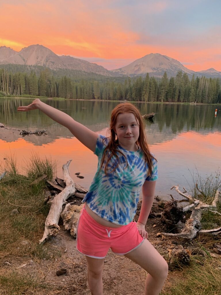 Cameron standing on the shores of Manzanita Lake at sunset. With a bright red sky and a perfect mountain reflection in the lake.