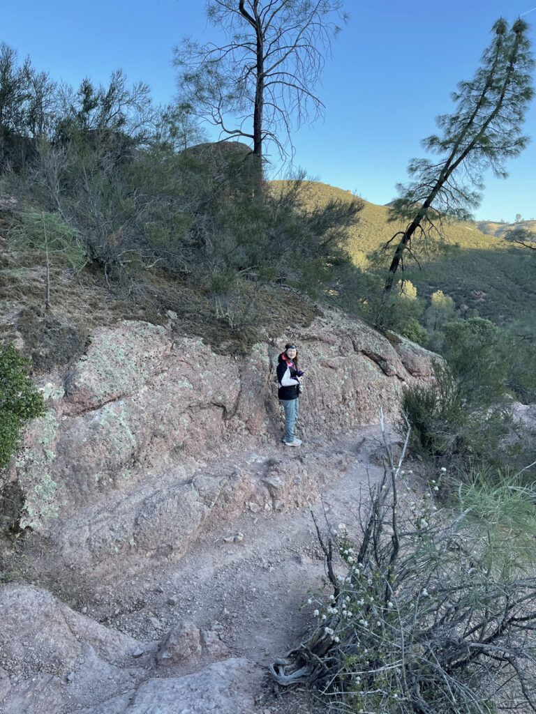 Cameron looking back at me from a distance as she hikes the narrow and rocky section of the Rim Trail in Pinnacles National Park.