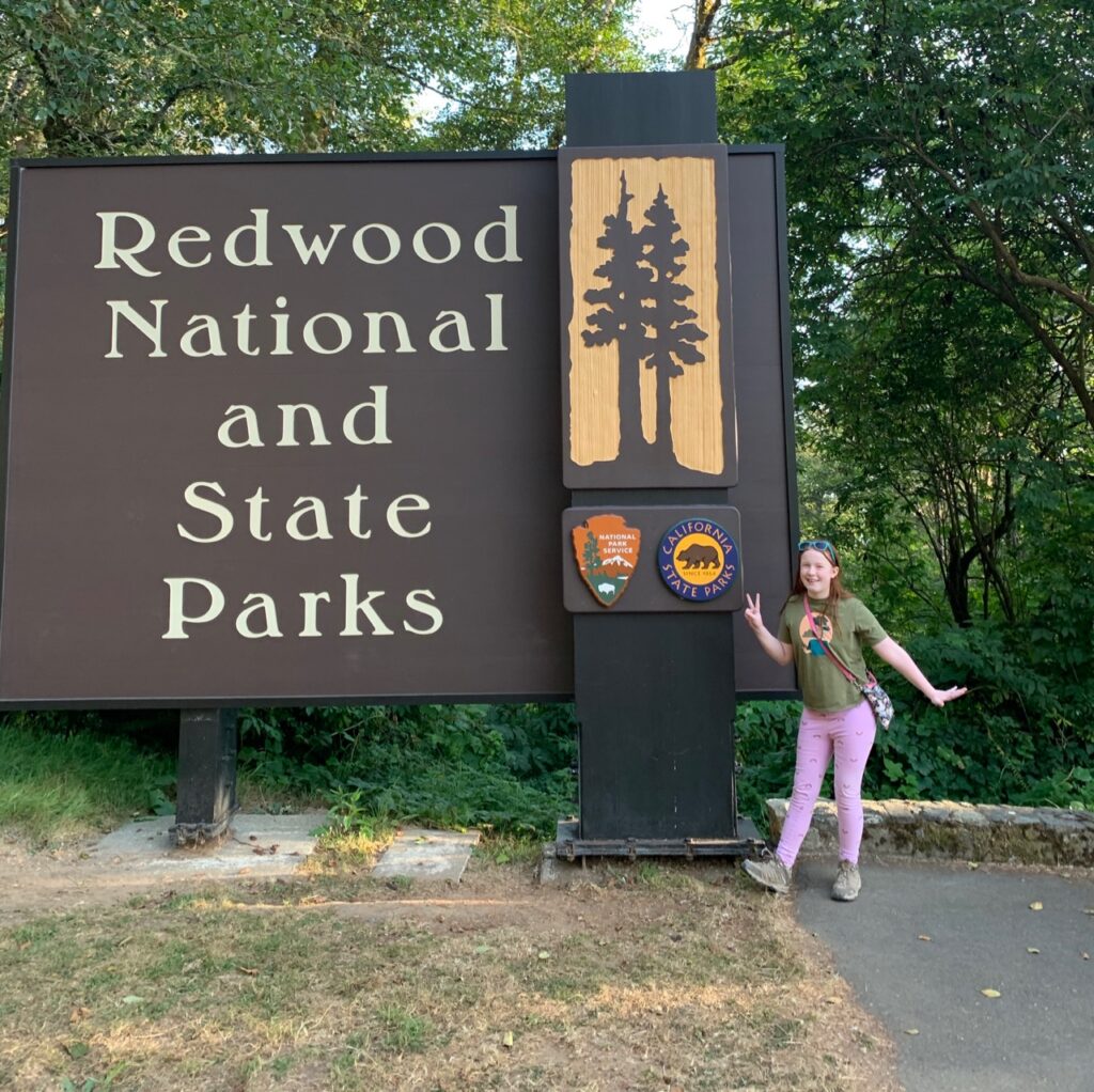 Cameron standing in front of the Redwood National and State Parks sign in California. 