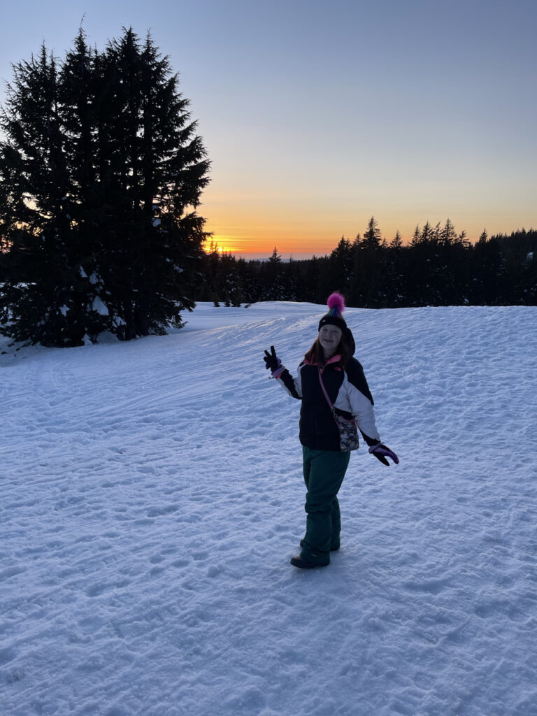 Cameron in full winter gear standing on top of almost 30 feet of snow in Crater Lake National park. Making a peace sign and smiling. 