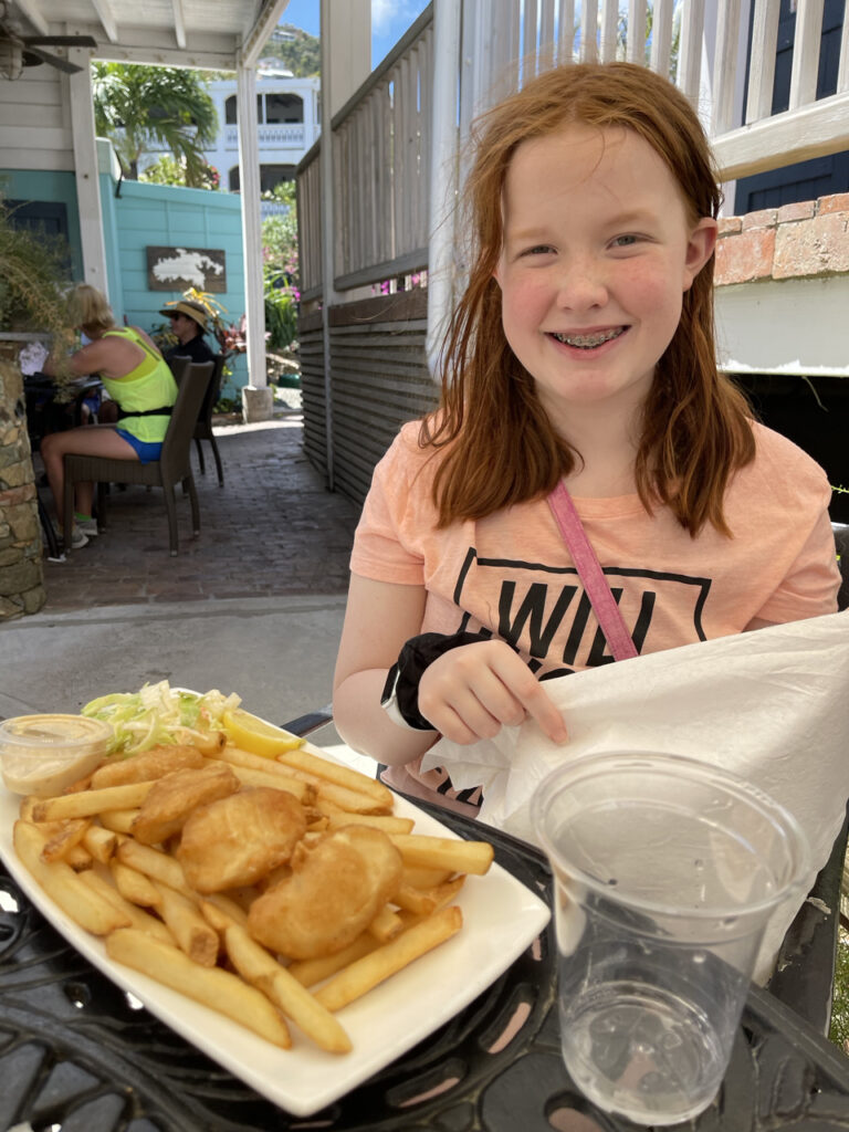 Cameron my daughter sitting at an outdoor dinning table in the Virgin Islands about to eat her plate of Fish and Chips thats in front of her. Taken near the Cocoloba Shopping Center.