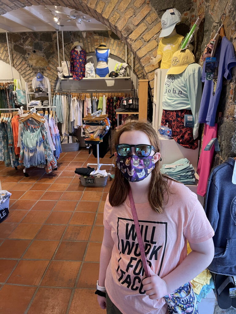 Cameron shopping at a gift store in the Virgin Islands wearing a shirt that says "will Work for Tacos" and wearing sunglasses and a mask inside.