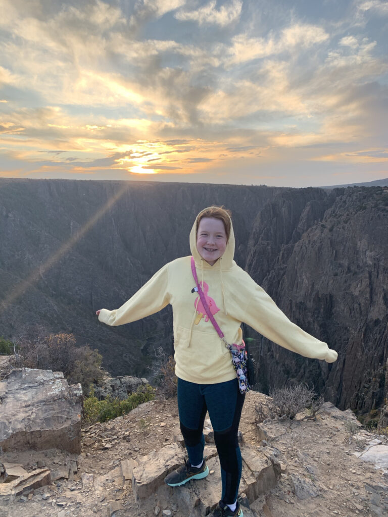 Cameron standing at sunset at the Big Island View in the Black Canyon of the Gunnion National Park. The sky is just turning yellow at sunset.