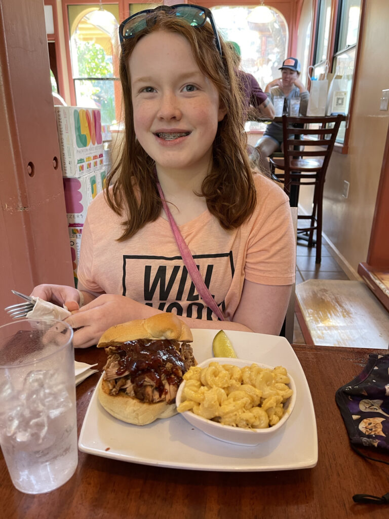 Cameron in a restaurant in the US Virgin Islands eating a pulled pork sandwich, and mac and cheese. At a high top table for lunch.