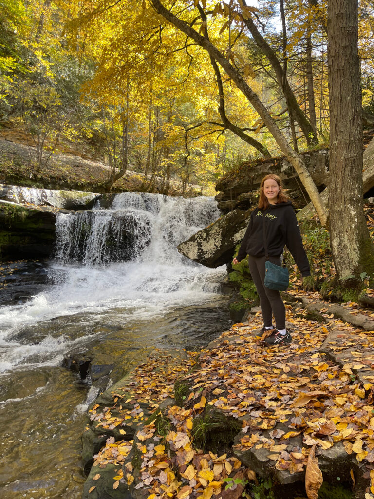 Cameron all smiles as she stands on a massive pile of wet leaves next to a small put rushing waterfall on the Dunloup Creek, in New River George National Park. 