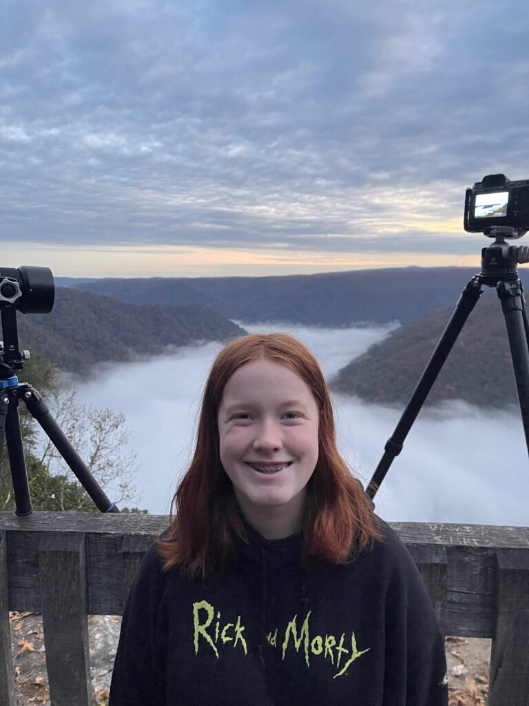 Cameron at sunrise at the Grand View Overlook in New River George National Park. There is a cloud inversion behind and below here that has filled the narrow valley (george) with clouds. The trees that can you can see are full of color at the peak of fall. 