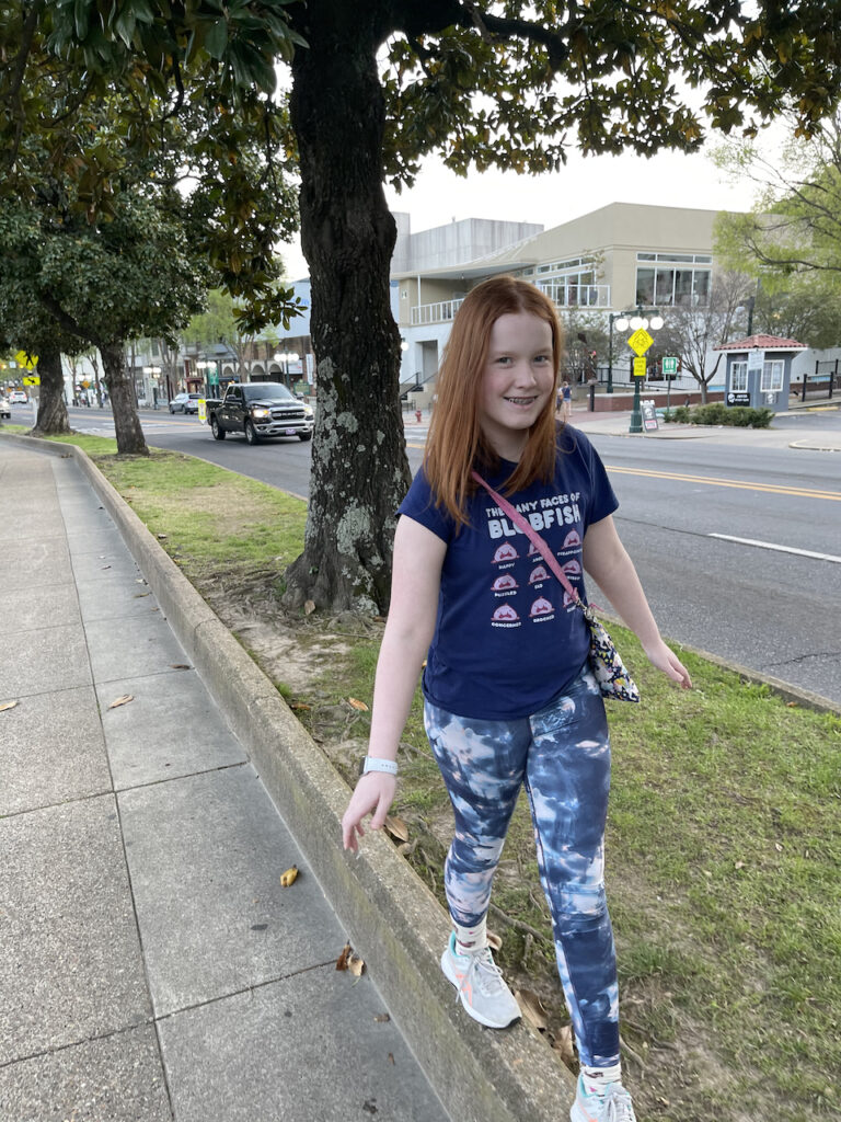 Cameron smiling while walking on a very tall curb that is next to the side walk off the main street where all the bathhouses are.