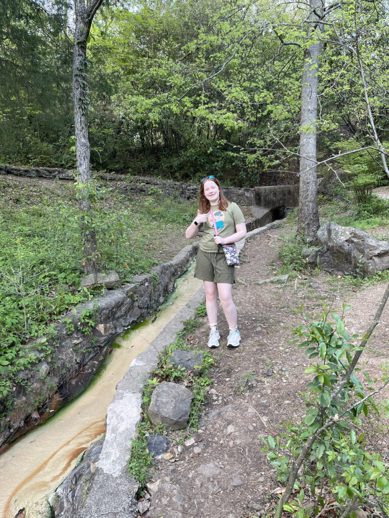 Cameron giving me a thumbs up as she poses for a photo in the woods of Hot Springs National park next to a massive channel of water that has been created to move the spring water down to town.