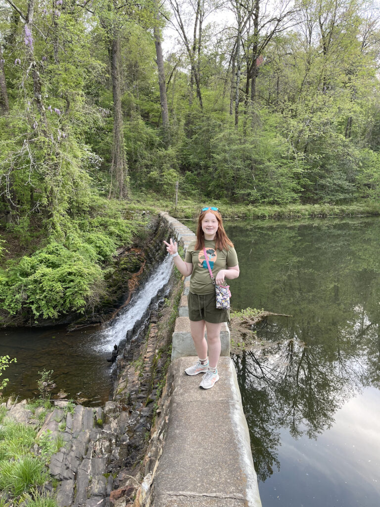 Cameron in a green shirt and black shorts standing on the dam of Destro Lake.