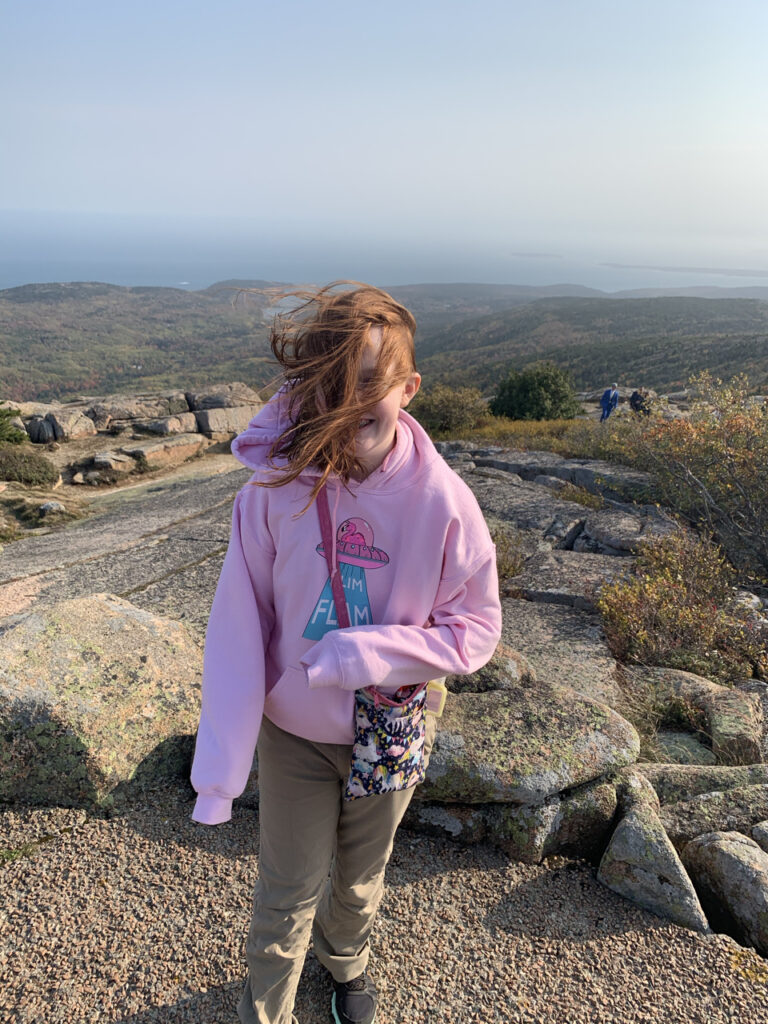 Cami standing on top of Cadillac Mountain in Acadia National Park. Her hair is blowing all over as the wind gusts where intense. 