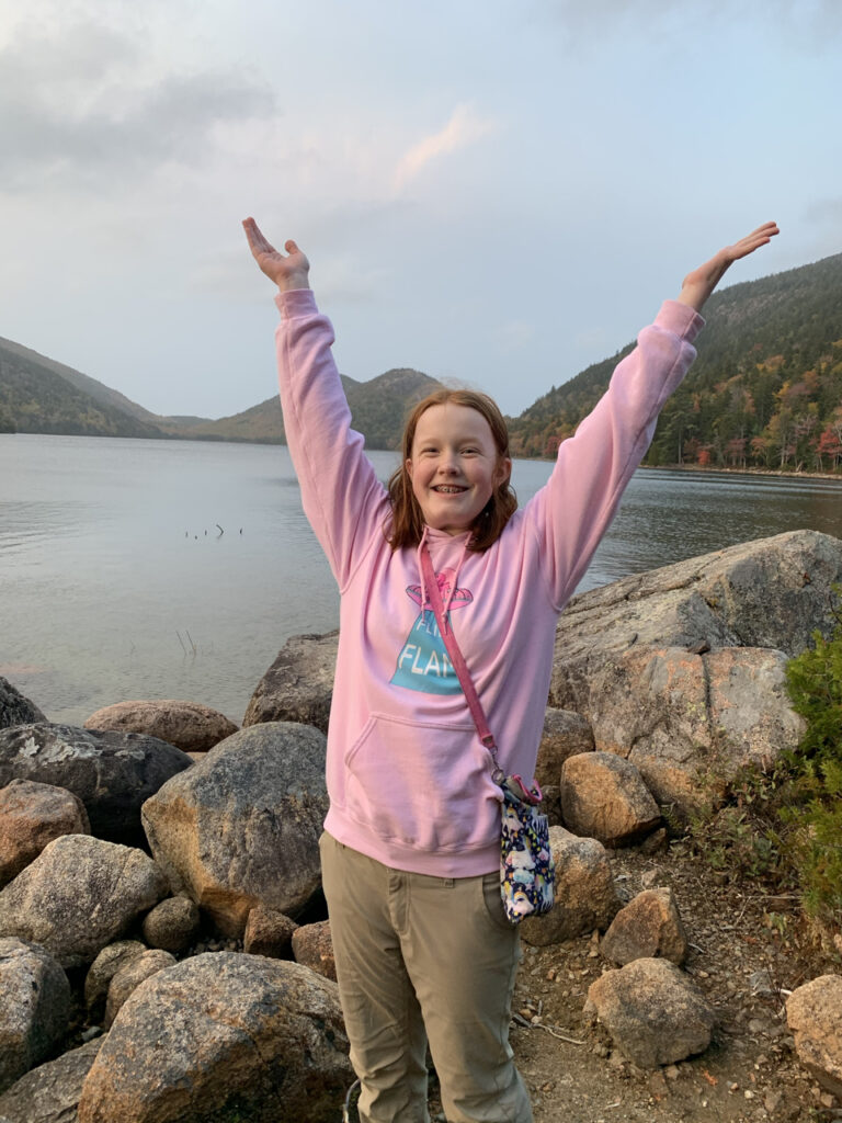 Cameron smiling with her arms up in the air while playing on the rocks on the shores of Jordan Lake.