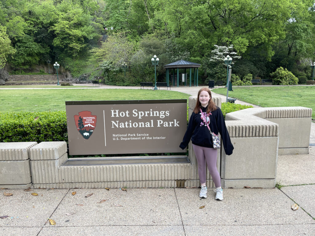 Cameron standing in front of the Hot Springs National Park sign wearing a hoodie and leggings. 