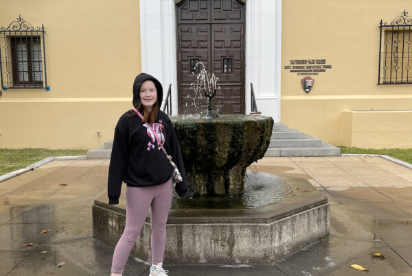 Cameron standing next to a massive Decorative Fountain that is spraying up hot spring water outside one of the very old Park Buildings that used to be a bath house.