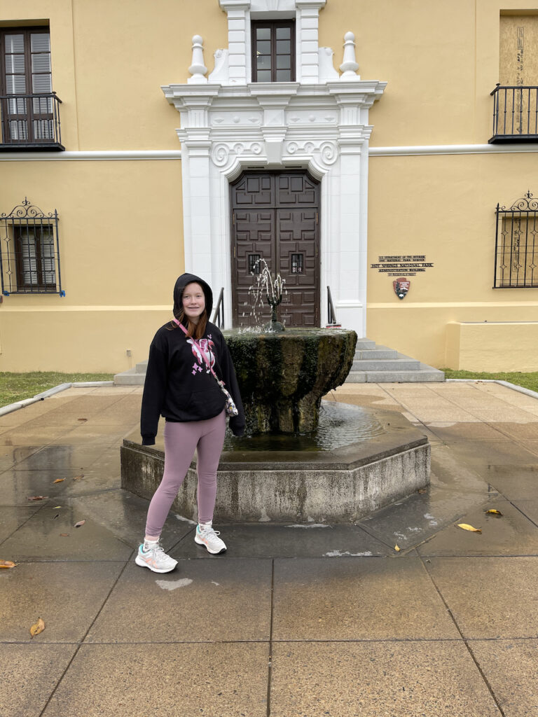 Cameron standing next to a massive Decorative Fountain that is spraying up hot spring water outside one of the very old Park Buildings that used to be a bath house.