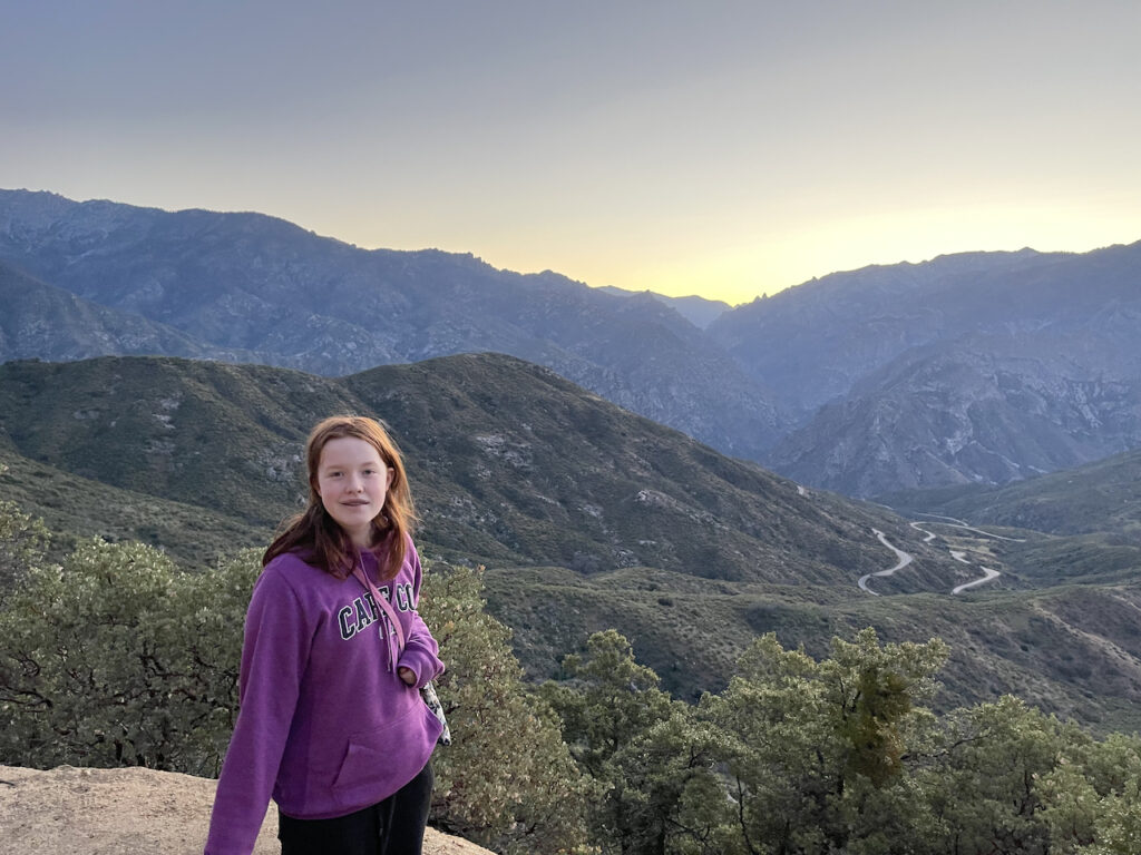 Cameron at an unnamed overlook in Kings Canyon enjoying the view down to the valley below and the mountains in the distance. Her red hair is glowing for the sunset light.