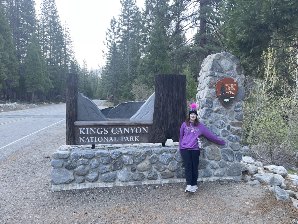 Cameron standing in front of the Kings Canyon National Park sign wearing a hoodie and a hat.